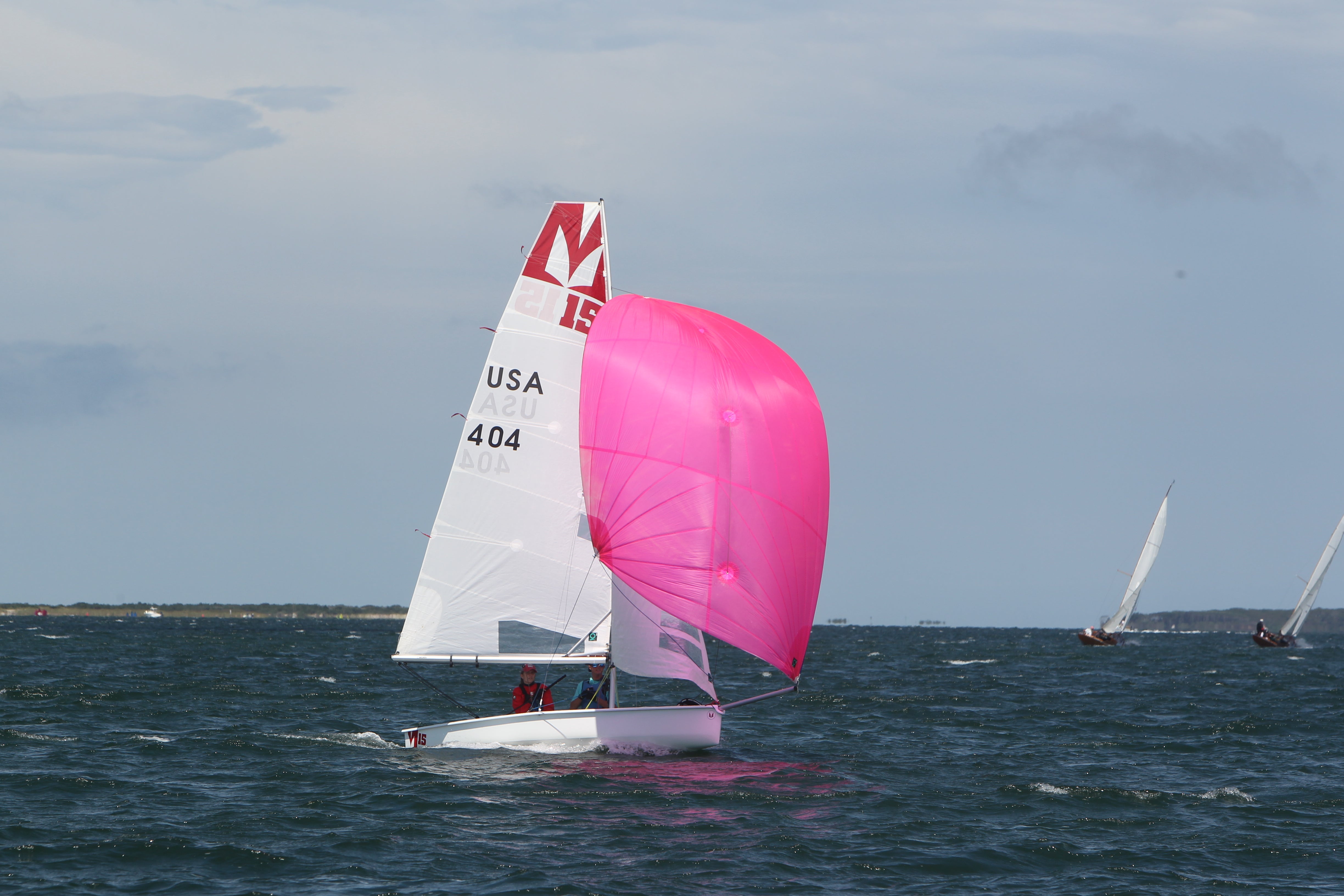 Sailboat with a pink sail on a body of water under a clear sky